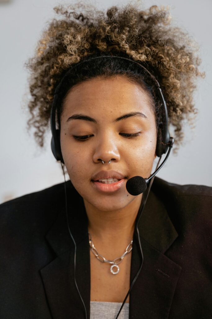 Close-up of a young woman with curly hair wearing a headset, engaged in customer service.